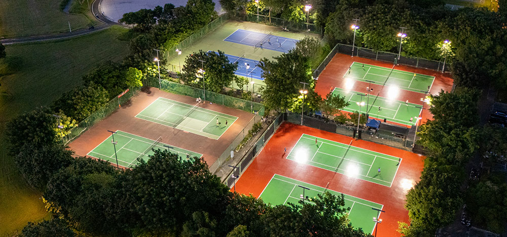 Tennisplätze bei Nacht mit Flutlichtanlage umgeben von Wald