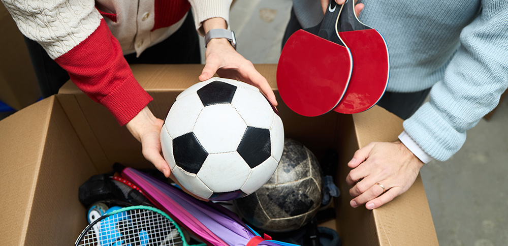 Zwei Personen sortieren gebrauchte Sportgeräte aus einer Kiste aus